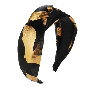 Detailed macro view of metallic golden bat prints on black knotted Halloween headband