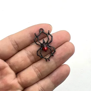 Nahaufnahme eines schwarzen Metallspinnen-Anhängers mit rotem Kristallkörper für Halloween DIY-Schmuck.
