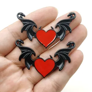 Primo piano dettaglio di ciondoli metallici con ali cuore diavolo gotico, lega nera e rossa.