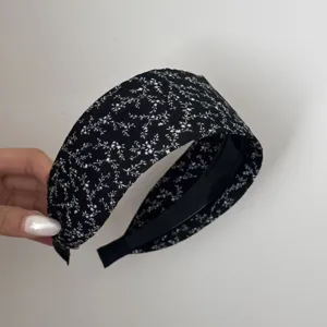 Detail view of a wide black floral headband showing fine white pattern and quality fabric.
