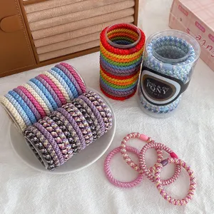 Detailed view of colorful braided hair ties in transparent storage cans, elastic scrunchies.