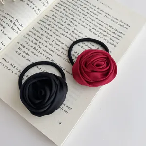 Close-up detail of exquisite fabric rose hair ties in black and red on book background.