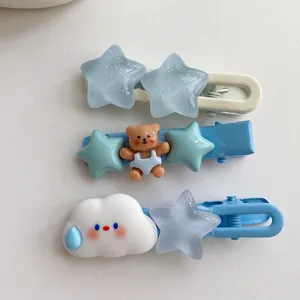 Primo piano dettagliato di simpatici fermagli per capelli blu con stelle, orsetto e nuvola.
