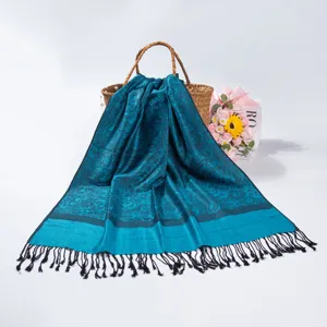 Detailed drape of teal paisley jacquard pashmina scarf with tassels on basket.