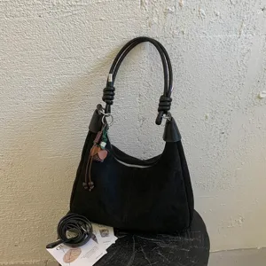 Détail de sac porté épaule en suédine noire avec poignée nouée, poche zippée et forme hobo souple.