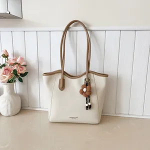 Detailansicht der lässigen großen Handtasche mit eleganten Trägern und süßem Blumen-Anhänger.