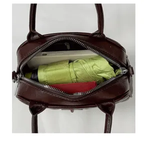 Brown leather top handle handbag showcasing interior capacity with phone and umbrella.