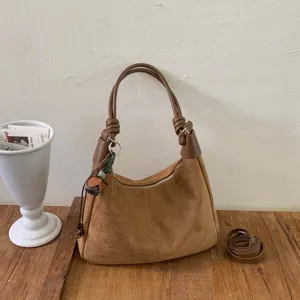 Gros plan du sac porté épaule en suède marron avec poignée nouée et détail zippé.