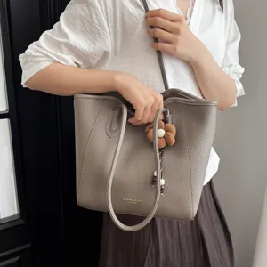 Detailaufnahme der grauen Leder Tote Bag mit feiner Textur, Schulterriemen und Blumen-Charm.