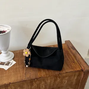 Vue détaillée du sac porté épaule en suédine noire avec charm fleuri, texture du tissu.