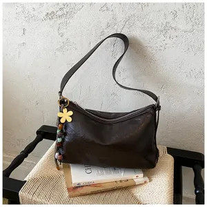 Close up of dark brown leather shoulder bag detail with cute metal flower charm and strap.