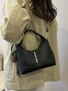 Black leather hobo shoulder bag with metal lock closure worn by model for daily casual chic.