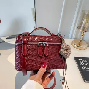 Primo piano della borsa intrecciata bordeaux, cerniere metalliche e tracolla elegante e chic.