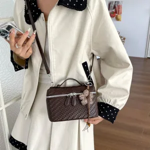 Scatto dettagliato di una borsa a tracolla intrecciata marrone con ciondolo floreale.