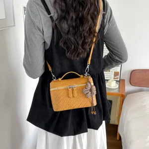 Vista dettagliata dell'elegante borsa a tracolla intrecciata gialla con manico e ciondolo.