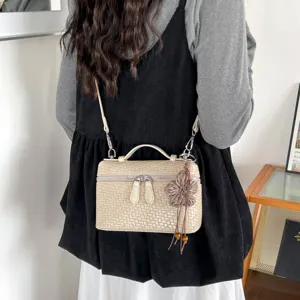 Primo piano della borsa a tracolla intrecciata beige con ciondolo floreale e manico elegante.