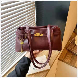 Detailansicht der eleganten burgunderroten Ledertasche mit goldenem Metallverschluss und Anhänger.