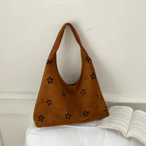 Vista di dettaglio della borsa hobo marrone in camoscio con fiori intagliati e libro.