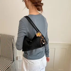 Detailansicht der schwarzen Wildleder Umhängetasche, modische Achseltasche mit Blumenanhänger.