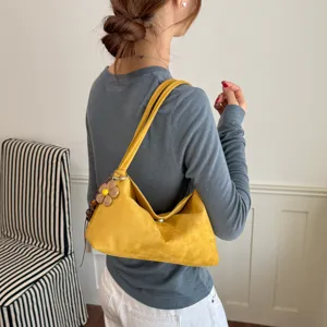 Detailansicht einer stilvollen gelben Wildleder-Schultertasche mit süßem Blumen-Anhänger.
