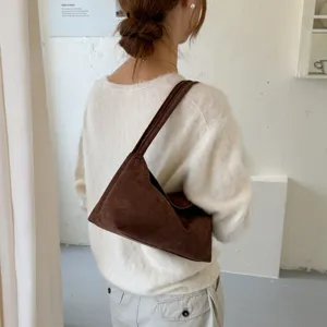 Détail de sac porté épaule en daim marron minimaliste, sac axillaire de ville élégant pour femme.
