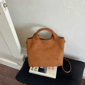 Vista detallada de un bolso tote de ante trenzado marrón con textura exquisita y diseño elegante.