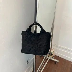 Vista detallada del bolso tote de cuero trenzado negro colgado en un perchero, textura.