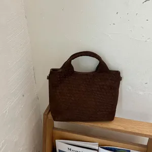 Primer plano del bolso tote trenzado marrón oscuro con textura elegante en escena minimal.