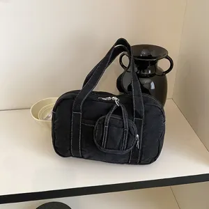 Detailed view of a black canvas handbag with white stitching and mini pouch charm on shelf.