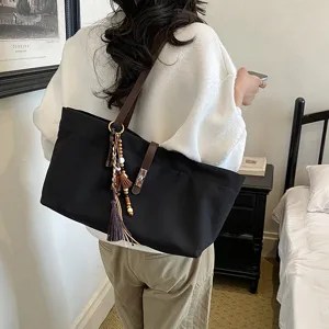 Detailed view of a stylish black large capacity tote bag with brown straps and tassel for women.