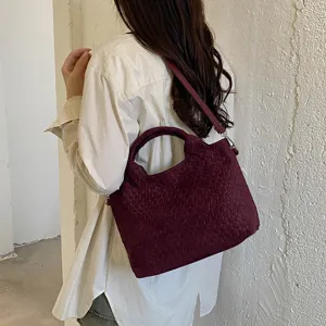 Vista detallada de un bolso de hombro tejido en rojo oscuro llevado por un modelo.