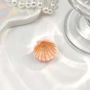 Makroansicht einer Mini-Haarklammer in Muschelform mit eleganten goldenen Linien.