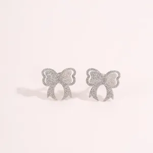 Detailed close-up of sparkling silver stainless steel bow earrings with glitter texture.
