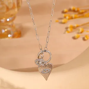 Close-up detail of silver paperclip chain necklace featuring evil eye and heart charm pendants.