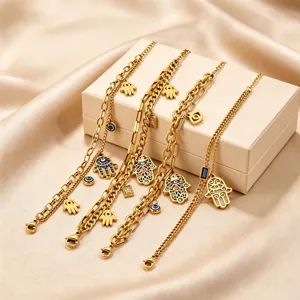 Close-up of gold stainless steel hamsa hand and evil eye charm chain bracelets detail view.