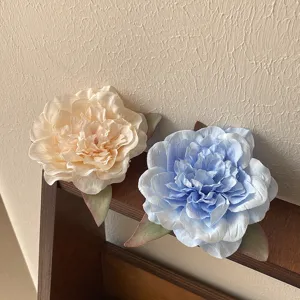 Close-up of large peony hair clips in beige and blue, displayed on a wooden rack.
