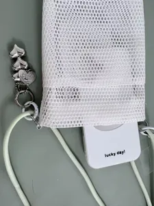 White mesh crossbody mini bag detail with silver heart charm and adjustable light green strap.