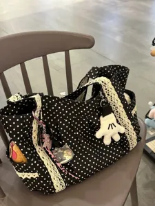 Detalle del bolso tote de lona con lunares blancos y negros, ribete de encaje vintage y colgante.