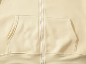 Close-up detail of beige zip-up hoodie featuring zipper and front kangaroo pocket texture.