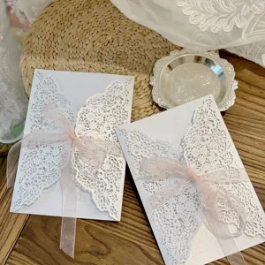 Détail d'une élégante carte d'invitation blanche découpée au laser avec dentelle et ruban rose.