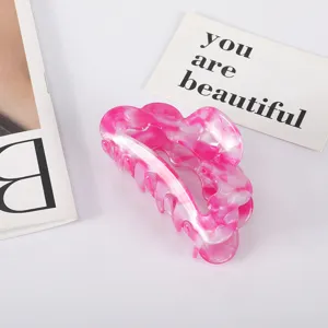 Macro view of a pink and white marbled acetate hair claw clip on a white surface.