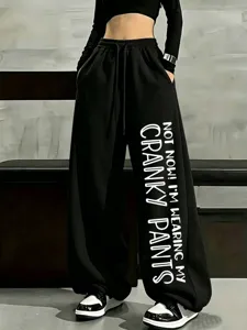 Detail view of black wide-leg sweatpants featuring bold vertical English print on leg.