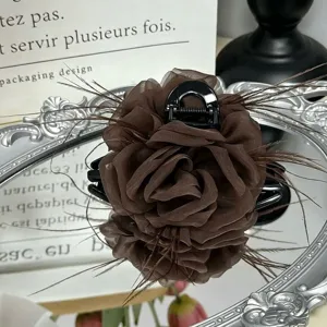 Detail shot of brown organza rose hair claw clip with delicate feathers on a vintage mirror.