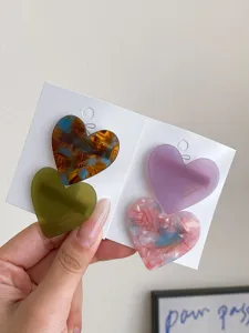 Detail shot of cute heart-shaped hair clips with colorful marbled and solid finishes on cards.