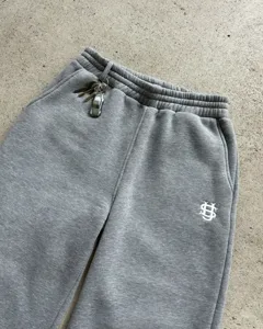 Grey streetwear fleece sweatpants detail showing embroidered logo and waist key accessory.