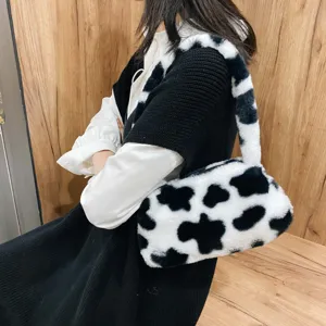 Close-up of a stylish cow print faux fur underarm bag worn on a model's shoulder.