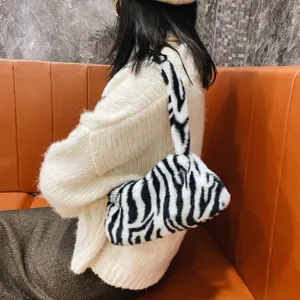 Side view of a stylish zebra print plush underarm bag worn with a white knit sweater