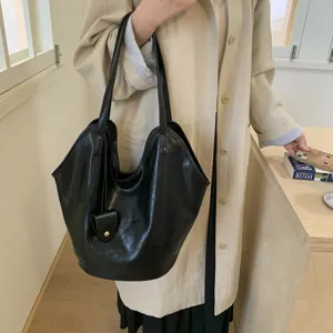 Large black slouchy tote bag worn with a beige trench coat for a minimalist look
