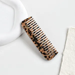 Dettaglio di un pettine a denti larghi in acetato con motivo leopardato su fondo bianco