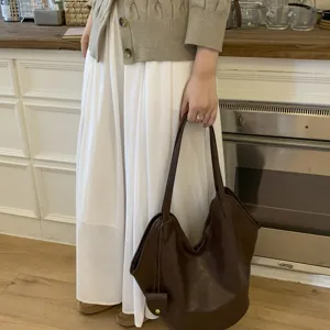 Minimalist dark brown leather tote bag held by a person in a cozy kitchen interior